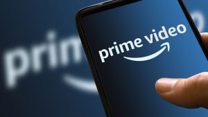 Prime video blue logo on mobile phone display with ramp color in the background. streaming movies and TV series platform icon on the smartphone screen holding hand. Italy, Milan, 24-01-22